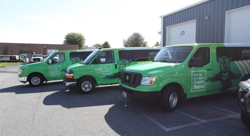 Three vans with green fleet wraps showing McDaniel College's logo and mascott