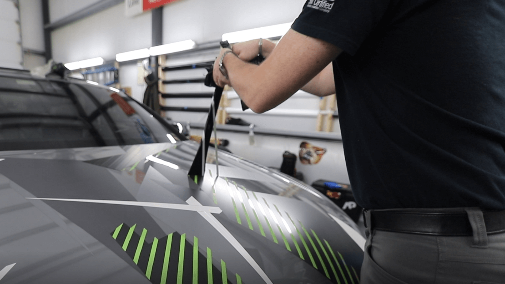 Technician removing vinyl wrap from a car hood in a shop