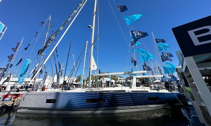 A side profile of a Beneteau yacht wrapped by AP Wraps, docked at a boat show marina surrounded by colorful flags and sailing enthusiasts.