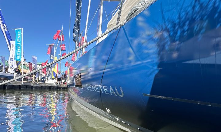 A side profile of a Beneteau yacht wrapped by AP Wraps, docked at a boat show marina surrounded by colorful flags and sailing enthusiasts.