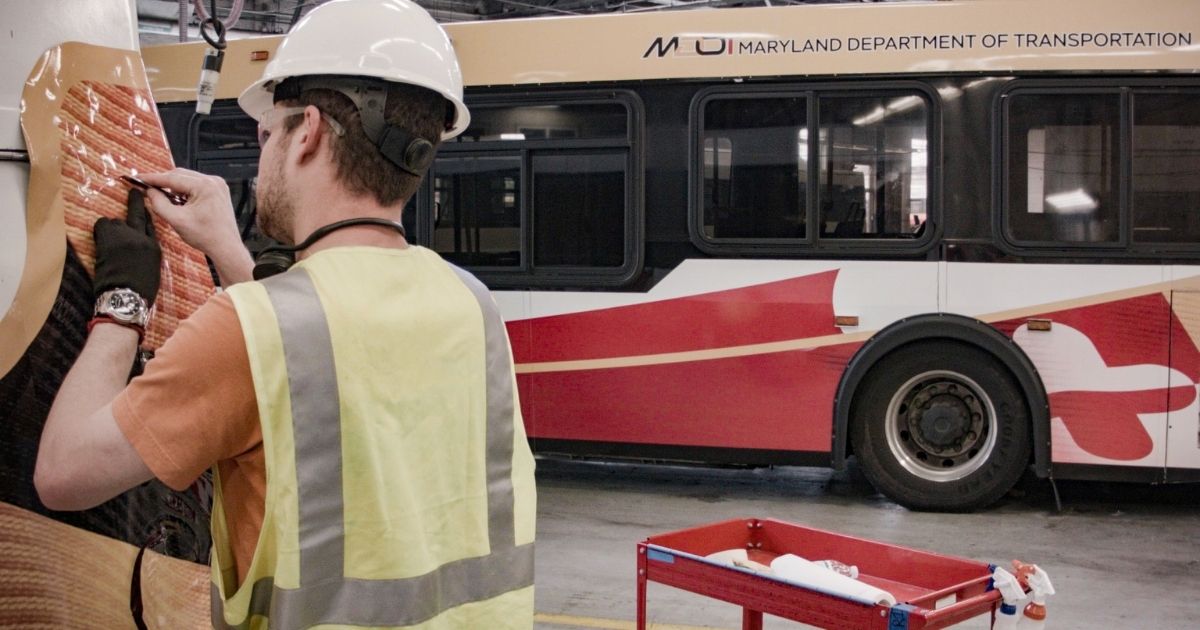 Technician applying a commercial vehicle wrap to a Maryland Department of Transportation bus