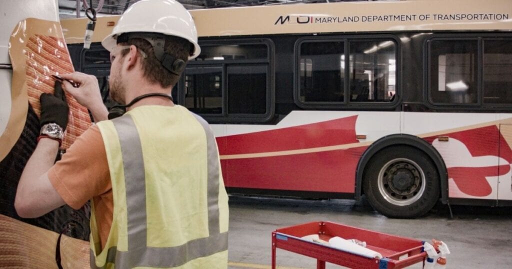 Technician applying a commercial vehicle wrap to a Maryland Department of Transportation bus